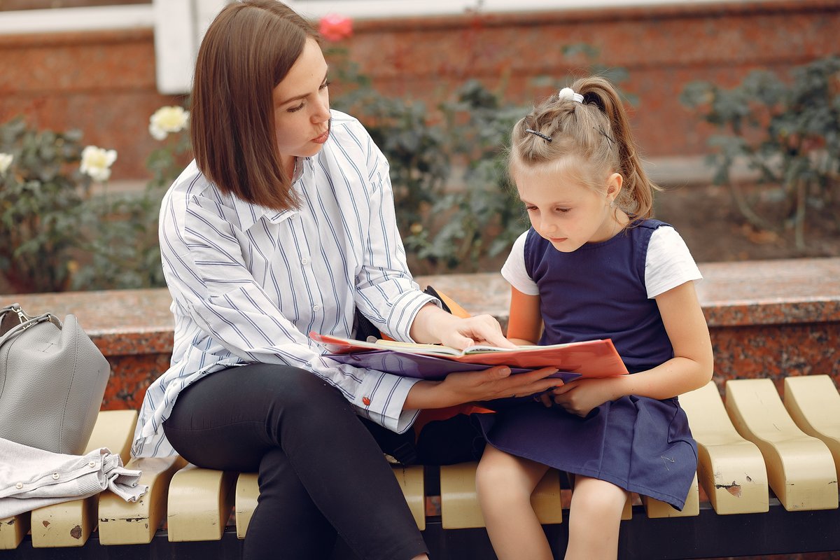 a kid trying to read with the help of her teacher a kid trying to read with the help of her teacher