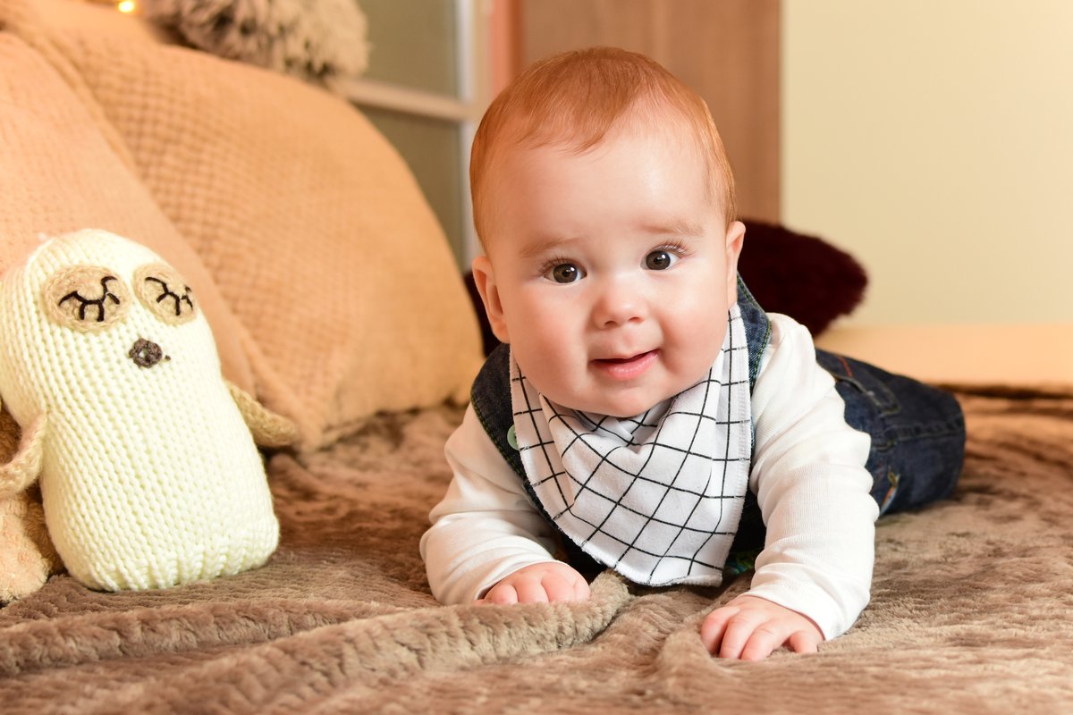 Bébé joyeux de 5 mois sur le ventre sur un tapis d'éveil au sol, tendant la main vers un jouet coloré Bébé joyeux de 5 mois sur le ventre sur un tapis d'éveil au sol, tendant la main vers un jouet coloré
